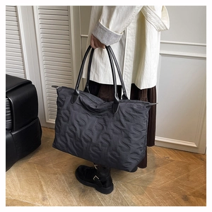 Detail of black tote bag featuring embossed S pattern and leather shoulder straps