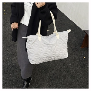 Detail view of light grey quilted tote bag with S-letter embossed texture and cream handles
