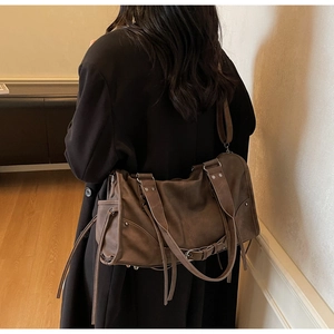 Détail du sac moto vintage marron foncé avec clous et lanières porté à l'épaule