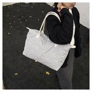 Detail of grey quilted tote bag with S-pattern embossing and cream leather handles