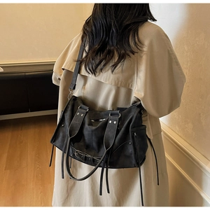 Detailed view of black vintage rivet shoulder bag worn with a beige trench coat