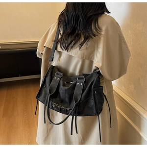 Détail du sac cabas rétro noir avec clous argentés et lanières porté sur un trench beige
