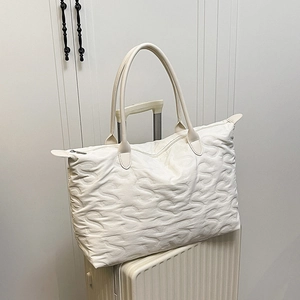Minimalist white quilted tote bag with S-letter pattern on a beige suitcase