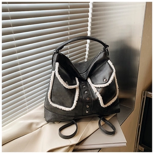 Detail of a vintage black faux leather bag featuring white faux shearling trim and rivets