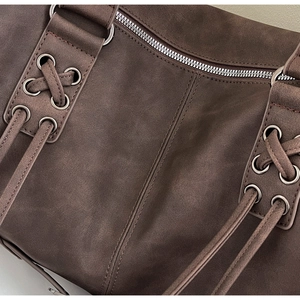 Détail du sac en cuir mat marron foncé avec fermeture éclair argentée et laçage croisé