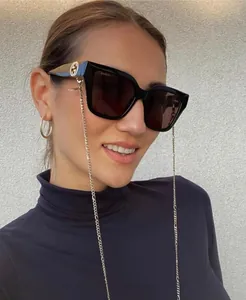 Detail of square black sunglasses with gold interlocking logo and matching eyewear chain