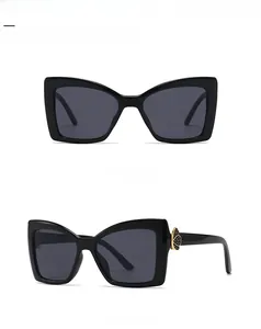 Lunettes de soleil à monture noire épaisse avec détail papillon doré sur la branche