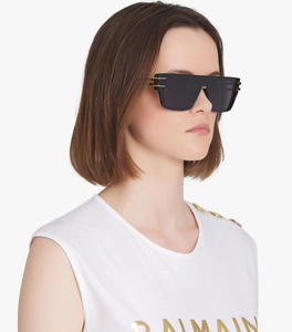 Detail of black oversized sunglasses with gold metal accents worn by a model