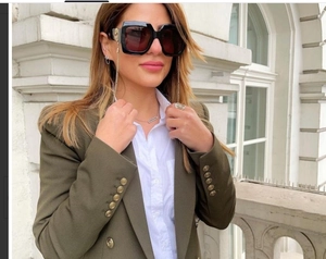 Dettaglio occhiali da sole quadrati neri con logo dorato e accessorio catena alla moda