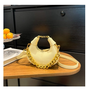 Detailed view of cream crescent bag with lychee texture and gold chain on wooden table