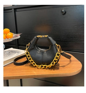 Detail of black pebbled leather crescent mini bag with gold chain on wooden table