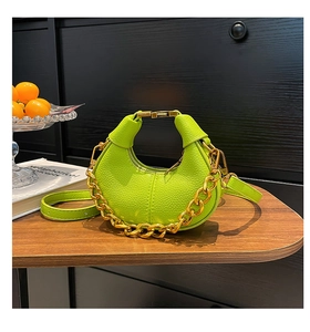Detail of neon green lychee leather crescent bag with chunky gold chain on wood