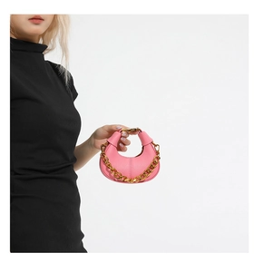 Close-up of pink crescent moon bag with pebbled leather texture and gold chain detail