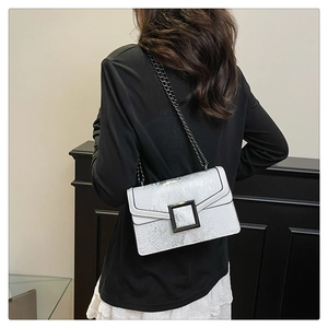 Sac argenté à motif serpent avec bandoulière en chaîne noire porté par un mannequin