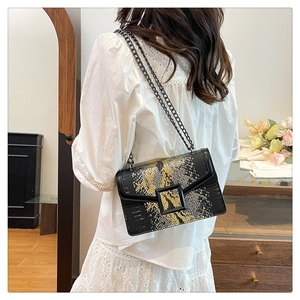 Détail du rabat à motif serpent et bandoulière chaîne sur un petit sac bandoulière noir