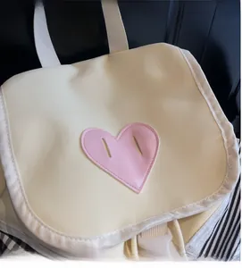 Detail of off-white backpack featuring a pink heart patch and white plastic buckle closure