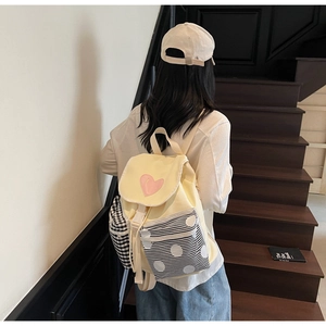 Detail of yellow canvas backpack showing pink heart patch and checkered side pocket