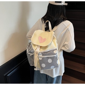 Close-up of yellow canvas backpack with pink heart, stripe and polka dot details on model