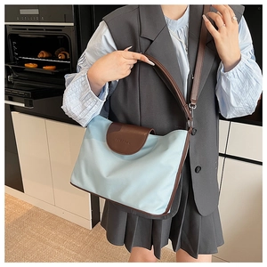 Detail of light blue nylon shoulder bag with brown leather flap and embossed logo