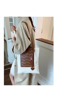 Detail of white canvas tote with laser-cut brown leather panel and heart charm