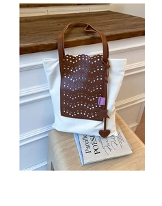 Detail of canvas tote bag with brown faux leather cutout pattern and heart pendant