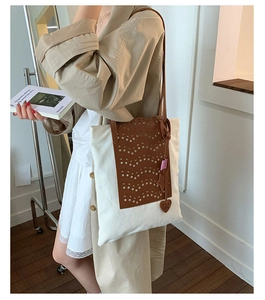 Detail of canvas tote with brown hollowed leather pattern and heart pendant on model