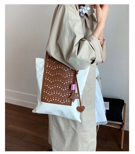 Detail of canvas tote bag featuring brown laser-cut leather overlay and heart charm