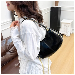 Detail of black crescent shoulder bag with gold rivets and chain strap on model