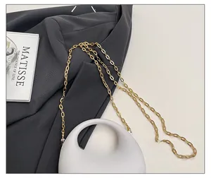 Detail of light gray minimalist handbag with elegant gold oval chain shoulder strap