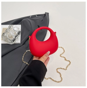 Detail of red acrylic handbag with gold chain strap against a professional blazer
