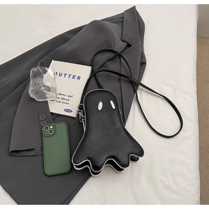 Minimalist black ghost-shaped crossbody bag with white eyes on a stylish studio setup