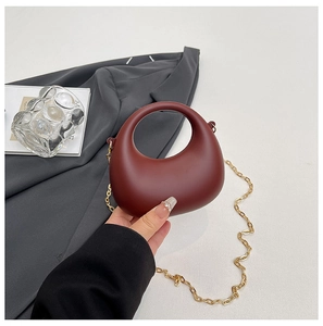 Detail shot of a burgundy acrylic handbag featuring round cutout handle and gold chain strap