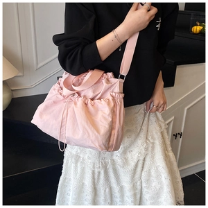 Detail of pink nylon bucket bag with drawstring closure and adjustable strap on a model
