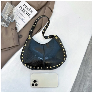 Macro shot of black pleated leather handbag with gold studs alongside a smartphone for scale
