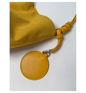 Detail of yellow suede bucket bag featuring knotted shoulder strap and round pendant charm