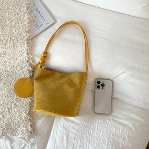 Detail of yellow matte suede bucket bag with round coin purse on a white minimal setting