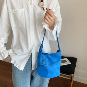 Detail of blue suede bucket bag featuring knotted strap and matching round charm pouch