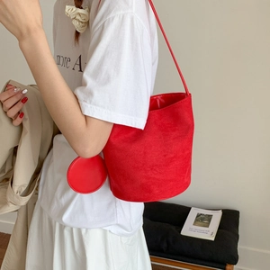 Detail of red suede bucket bag with matching round coin purse shown on a model shoulder