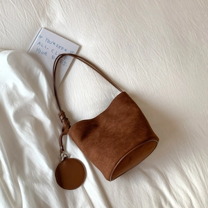 Detail of a dark brown suede bucket bag featuring a refined knot strap and circular pendant