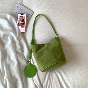 Close-up of green suede bucket bag with round coin purse on white fabric background