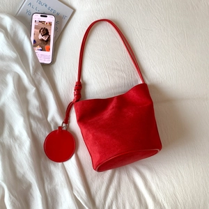 Detail of red frosted leather bucket bag with tied strap and round charm on white fabric