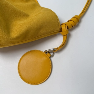 Detail of yellow suede bucket bag featuring knot shoulder strap and circular pendant