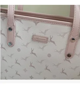 Detailed close-up of textured leather tote bag featuring pink reindeer prints and metal rivets