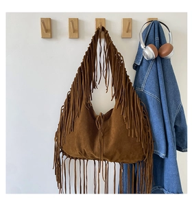 Detail of dark brown suede tote bag with long bohemian tassels hanging on a wall