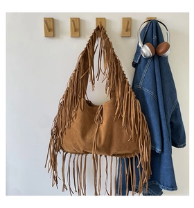 Detailed view of caramel brown suede hobo bag with long tassels hanging on wooden hook