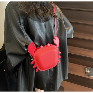 Detail of red crab-shaped crossbody bag in lychee pattern leather worn by a model