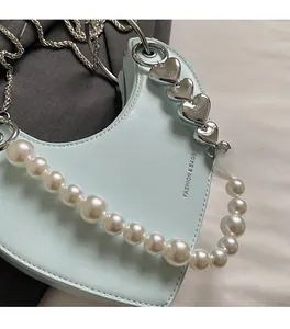 Dettaglio di una borsa azzurra a cuore con perle bianche e borchie a cuore argentate