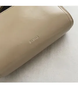 Dettaglio della fine trama della pelle e del logo SHISANG goffrato sulla borsa beige chiaro