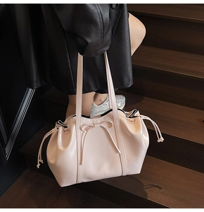 Detail of pink faux leather tote bag featuring ribbon bow and side drawstring accents