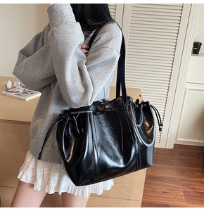 Detail of black glossy tote bag featuring a drawstring closure and ribbon bow decoration
